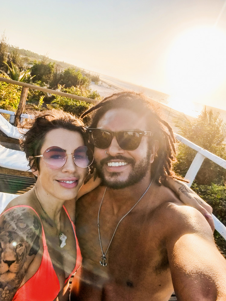 20210814_170431.jpg Imagem mostra mulher de biquini laranja e homem sem camisa, sorrindo, com um pôr do sol ao fundo.