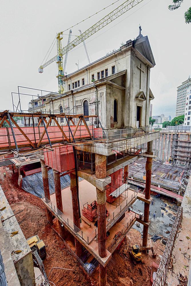 Foto mostra uma capela pendurada por diversas estruturas e ferros de construção