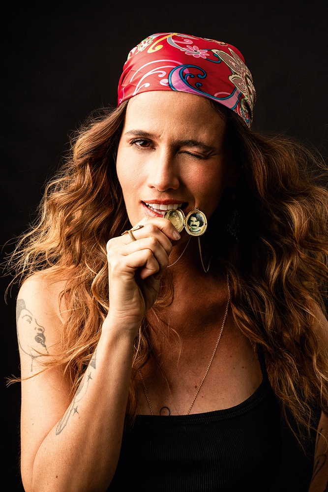 Cópia de AnaCañasCantaBelchior_FotoMarcusSteinmeyer_02.jpg Imagem mostra mulher com bandana vermelha mordendo colar com imagem de homem de bigode.