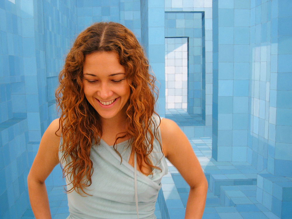 Adriana Varejão, artista plástica. Imagem mostra mulher sorrindo com pintura geométrica azulada ao fundo.
