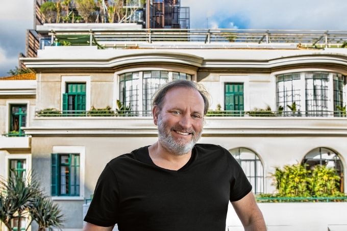 Alexandre Allard em frente a um prédio restaurado do Complexo Matarazzo. Ele está num terraço e dá para ver um pedaço do céu