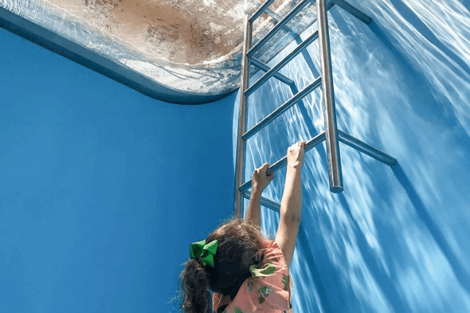 arte em 2022 Imagem mostra menina com os braços levantados segurando em escada de piscina, como se estivesse no fundo da água.