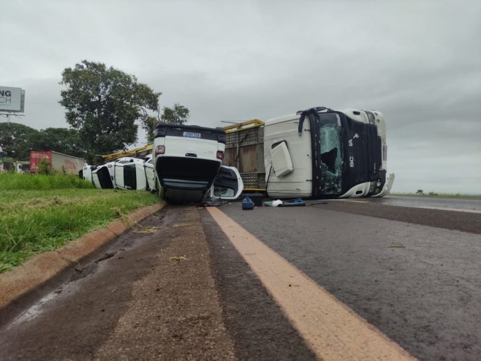 Imagem mostra um caminhão branco tombado, com os vidros quebrados, e outros 3 carros brancos também tombados em uma rodovia.