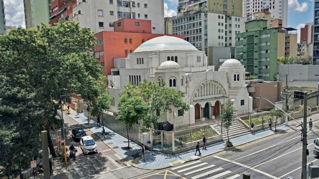museu judaico Uma foto um pouco longe de uma antiga sinagoga, com algumas árvores em volta e em um cruzamento