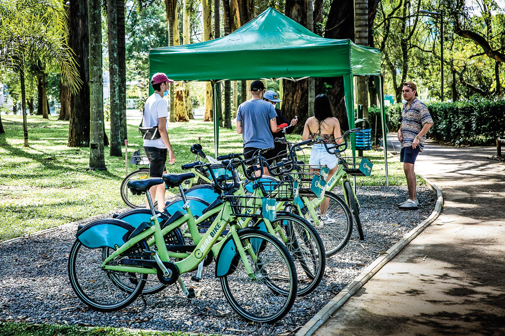São Paulo 09 dezembro 2021Flavio BikesFoto Alexandre Battibugli VSP Imagem mostra bicicletas da cor verde claro efileiradas. Ao fundo, árvores e pessoas caminhando.