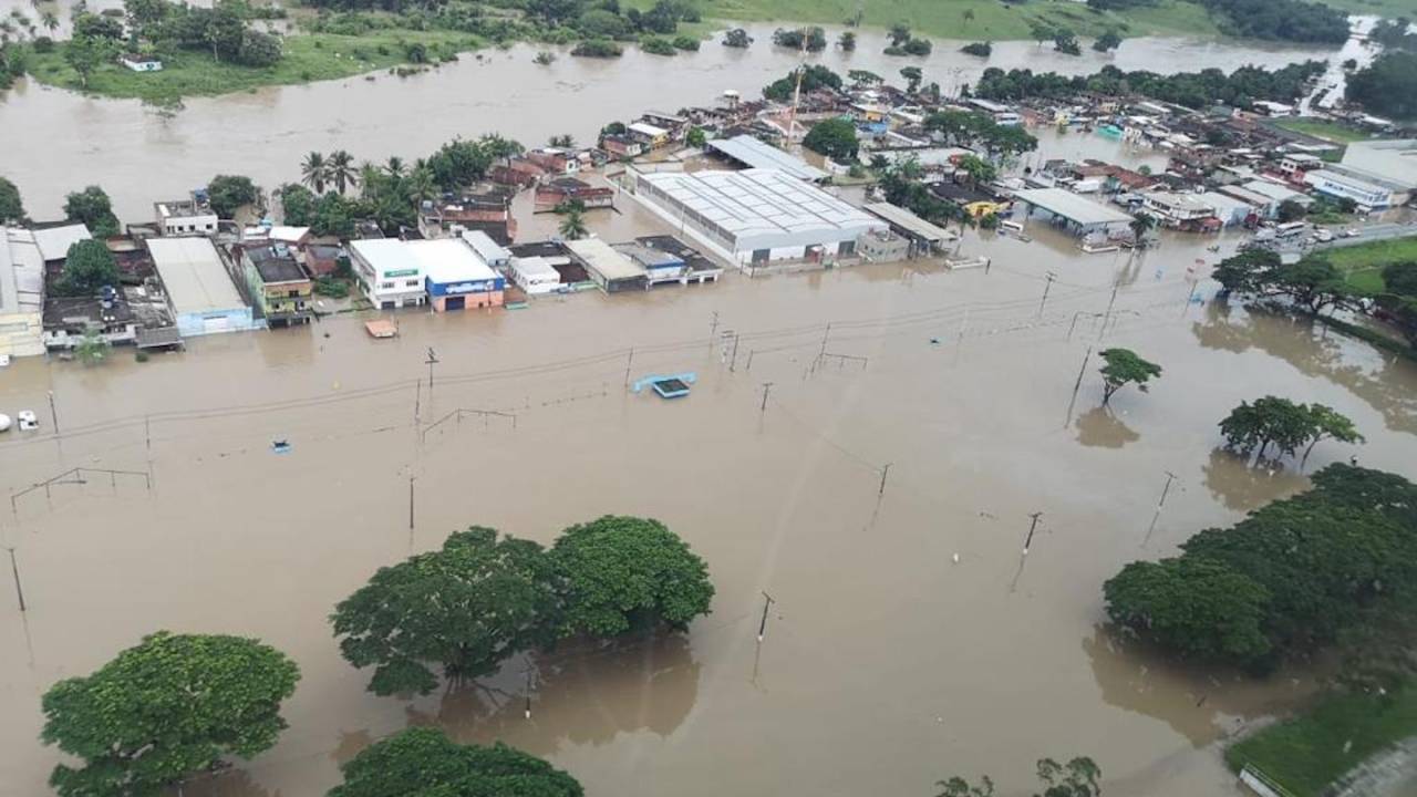 Imagem aérea mostra cidade alagada. Água tem cor marrom e está na altura das casas.