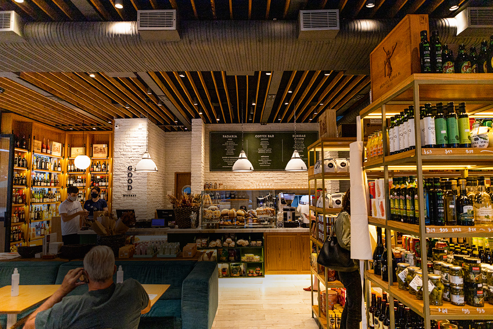 Ambiente de mercado com prateleiras preenchidas por produtos como vinhos, azeites e enlatados