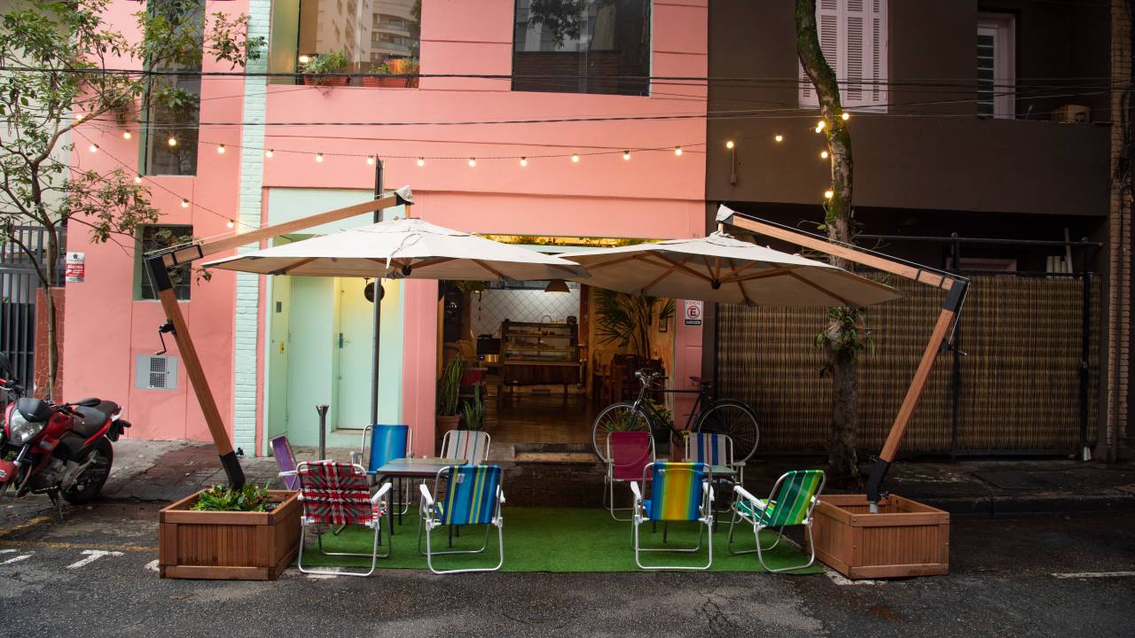 Fachada de bar pintada em claro tom de rosa. Na frente do estabelecimento, algumas cadeiras de praia e guarda-sóis podem ser vistos