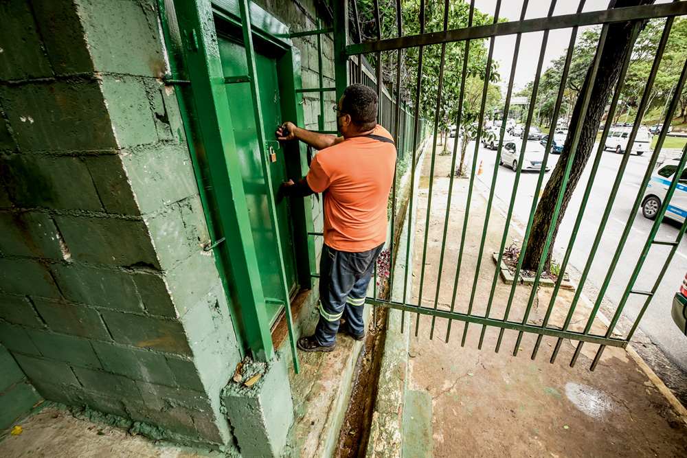 BUNKER_6.JPG Imagem mostra homem de camiseta laranja trancando porta verde com grades de segurança.