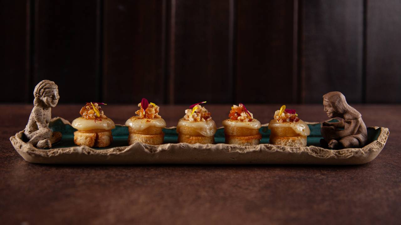 Porção de crostini de banana servida sobre bandeja com duas esculturas em suas pontas