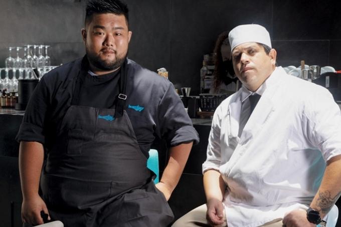 Seiji Enokizono e Wdson Vaz posam lado a lado vestidos em seus uniformes de cozinha