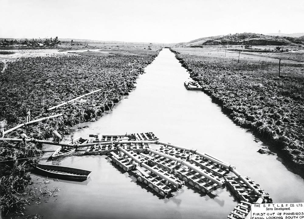Imagem em preto e branco mostra rio entre margens de grama.