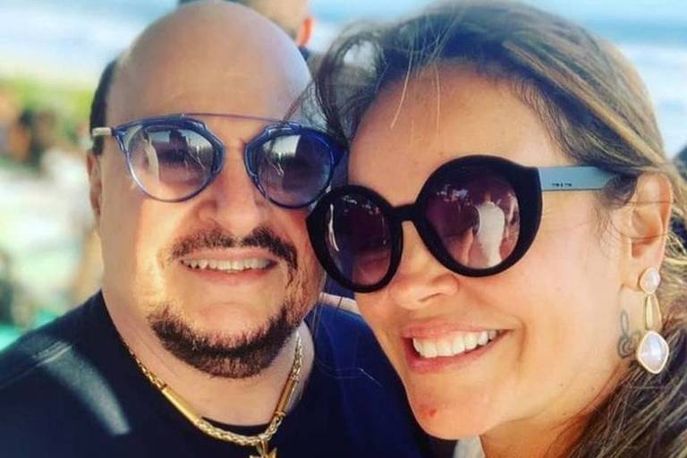 Paulinho, vocalista do Roupa Nova, e Elaine Soares Bastos sorriem para a câmera e usam óculos de sol.