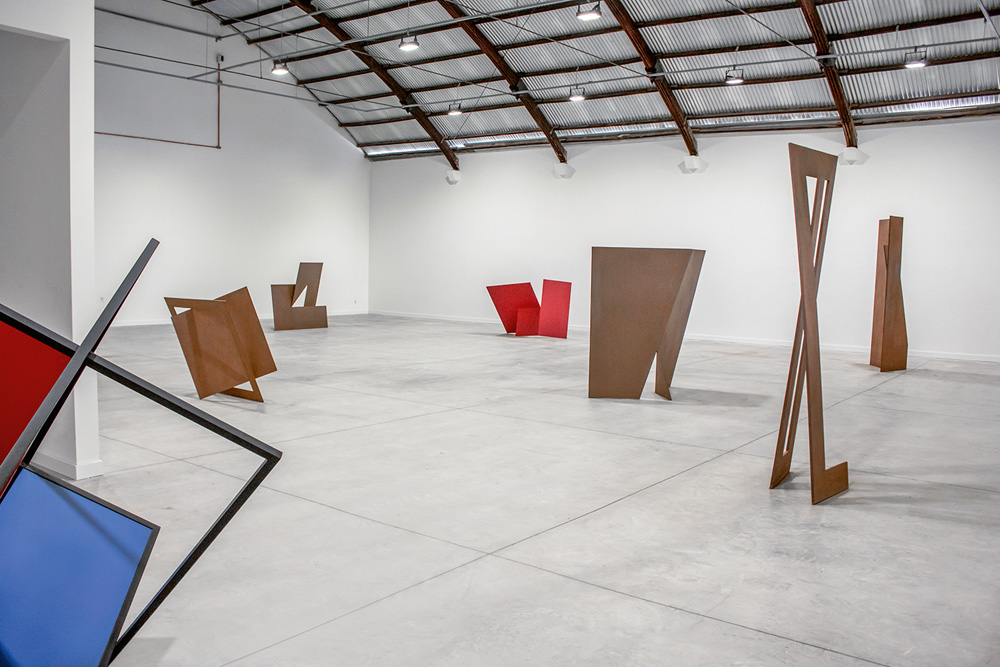 Peso 2-Créditos-João Cazzaniga.JPG Uma ampla sala de galeria com esculturas que lembram monumentos em formas geométricas, de quadrados e retângulos.