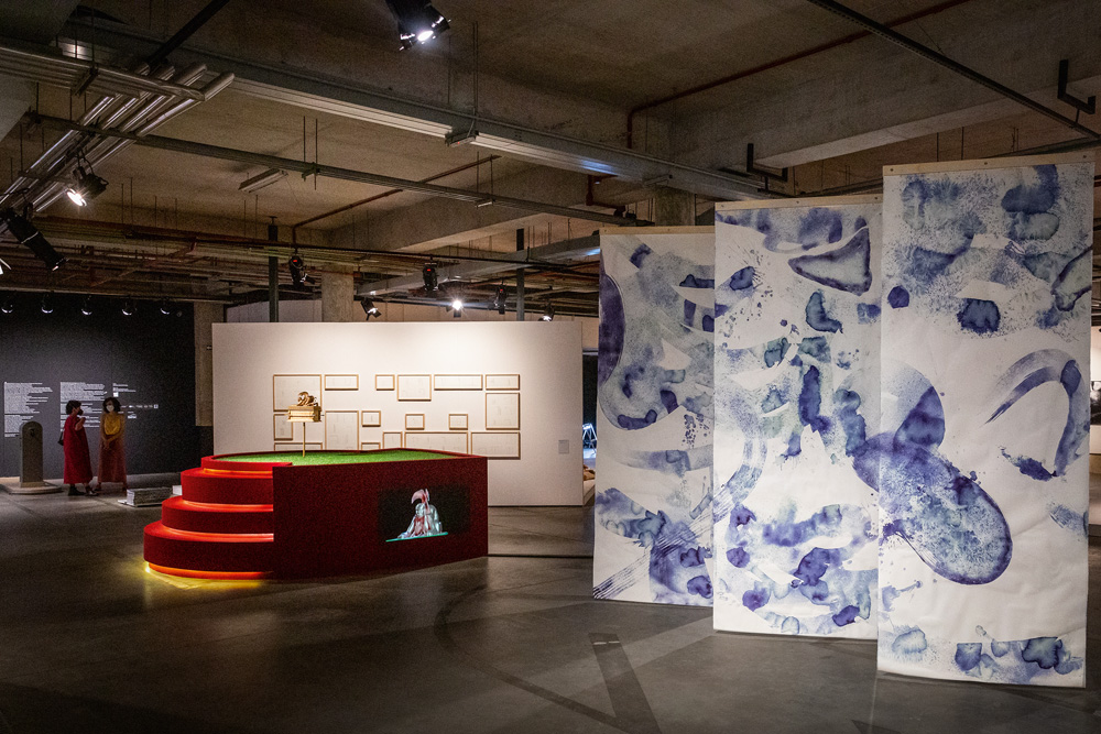 Foto mostra Trienal de Arte, em Sorocaba. Na imagem é possível ver uma ampla sala, com duas obras em destaque: um mural com pintura em tinta azul, que se posiciona à frente, e uma escultura que lembra um campo de futebol, ao fundo.
