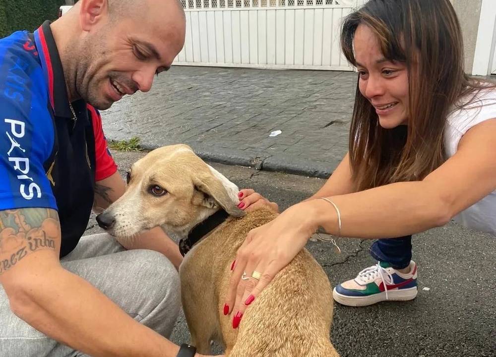 Reinaldo e uma moça se agacham para fazer carinho na cadela Pandora, no meio da rua.