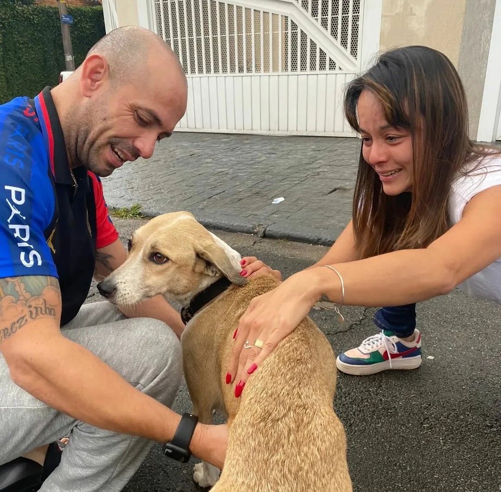 Reinaldo e uma moça se agacham para fazer carinho na cadela Pandora, no meio da rua.