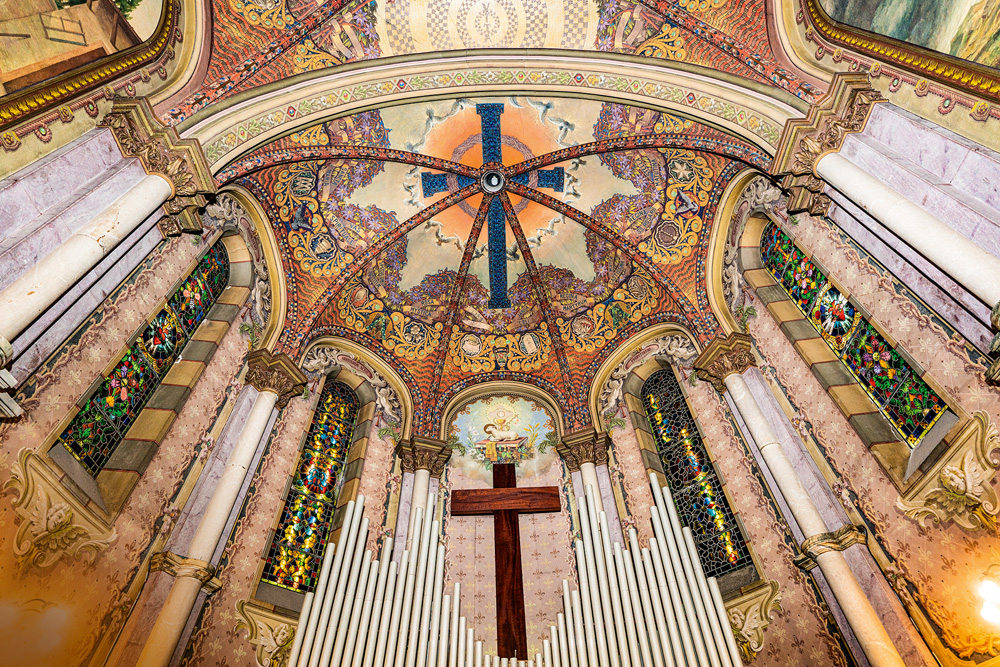 Sta Ifigênia crédito Marcelo Macaue.jpg Imagem mostra teto de igreja com uma cruz azulada ao centro e pinturas geométricas ao seu redor, coloridas. Nas laterais, vitrais também coloridos e, na parte inferior da imagem, uma cruz de madeira e alguns tubos de um orgão.