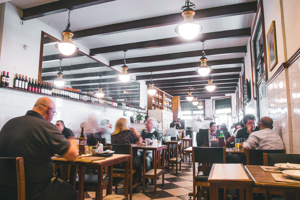 Ambiente de restaurante com espelhos na parede e garrafas de vinho como parte da decoração