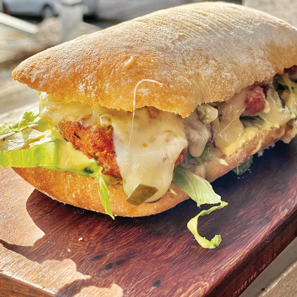 Pão tipo ciabatta cortado ao meio recheado por frango à milanesa e salada