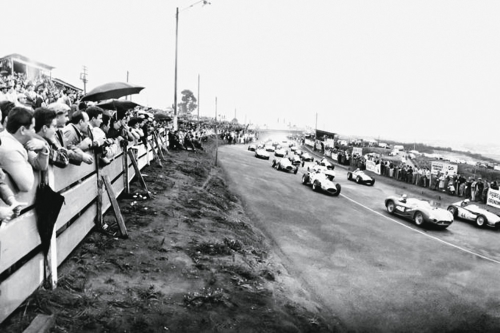 corrida-no-autc3b3dromo-de-interlagos-nos-anos-50_Reprodução A Saga dos Fittipaldi_Panda Books.jpg Imagem mostra carros de corrida em pista, à direita, e multidão atrás de barreira de madeira, à esquerda,