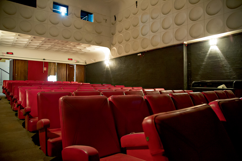 Veja SP Imagem mostra sala de cinema com poltronas de couro vermelhas e paredes brancas.
