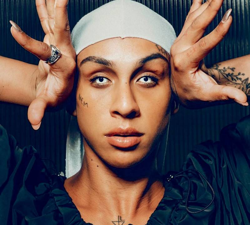 Retrato de Linn da Querada. Ela é um mulher negra, usa uma lente de contato branca e uma bandana branca que cobre os cabelos.