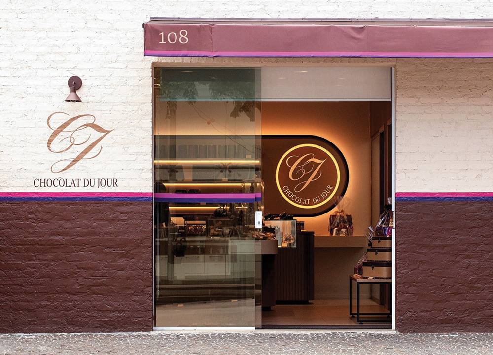 Fachada de loja com parede pintada de roxo e de branco. O toldo que cobre a porta de vidro também é roxo