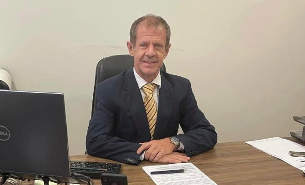 Imagem de Celso sentando em uma mesa. Ele veste um terno.