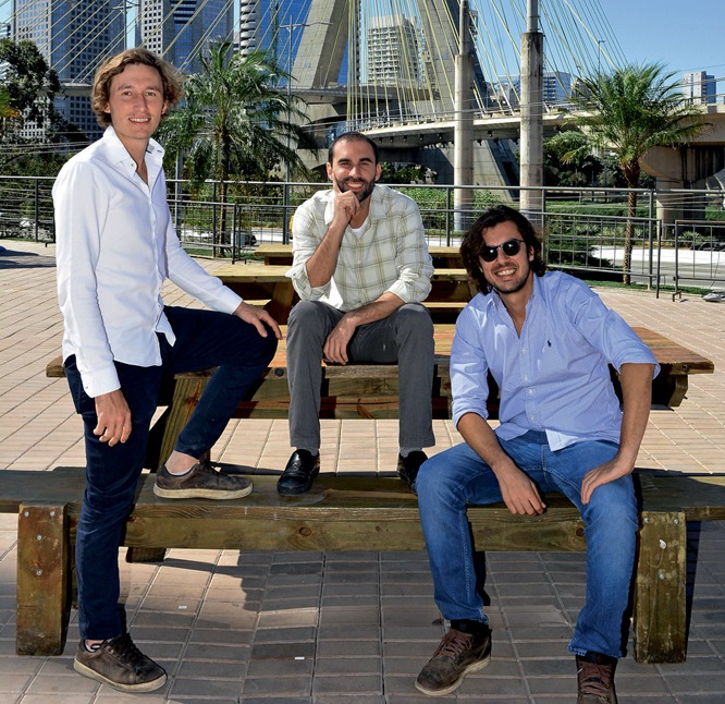 Bob Dannenberg, Thiago Armentano e Fernando Ximenes posam lado a lado, o primeiro de pé e os demais sentados. Ao fundo, a Ponte Estaiada.