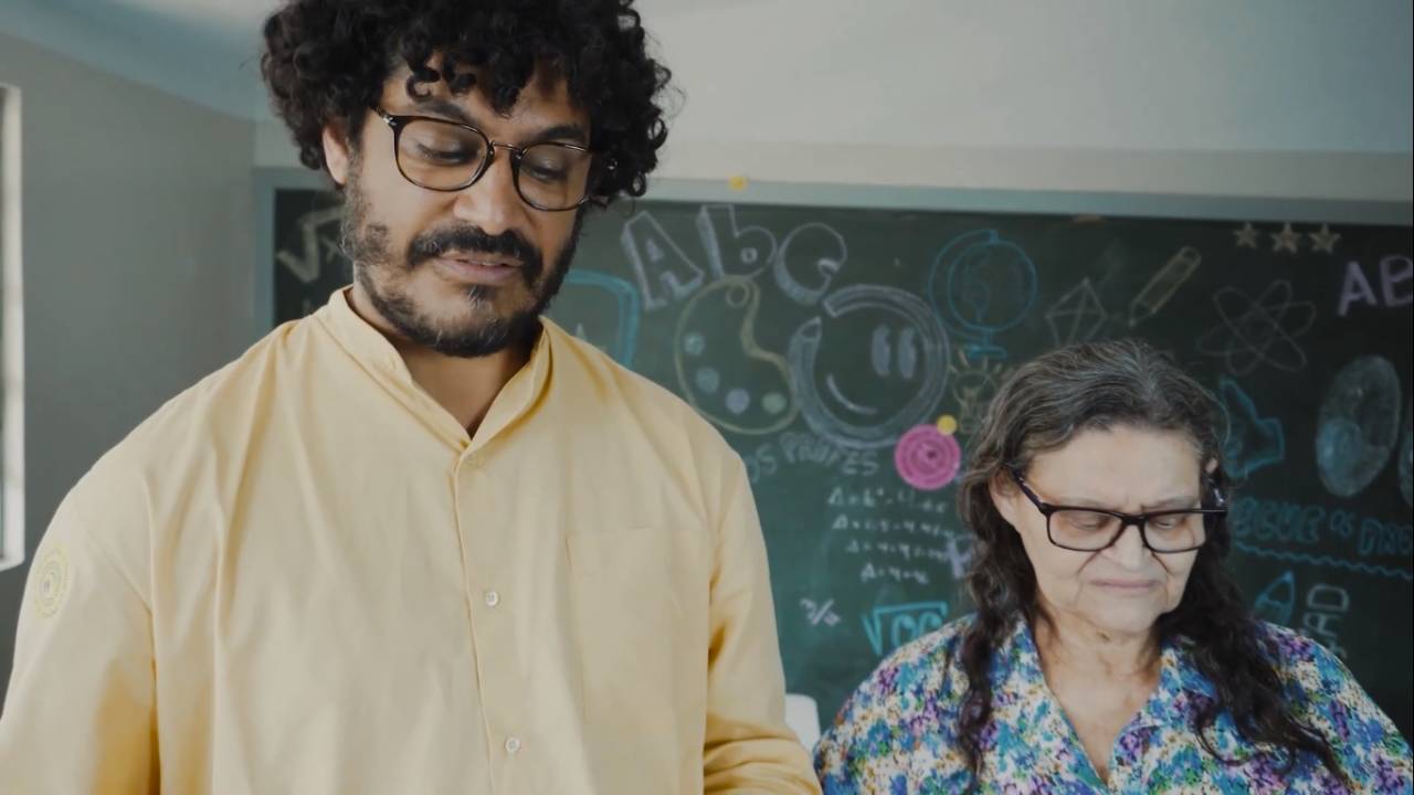 Criolo ao lado da mãe, Dona Vilani em sala de aula. Ele veste camisa amarela e ela camiseta estampada.