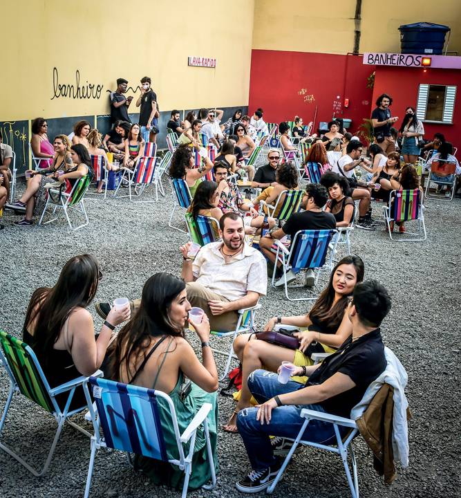 Jovens sentados em cadeiras de praia bebem em um estacionamento aberto.