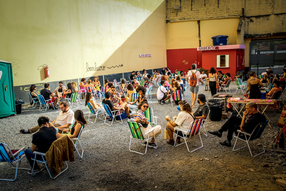 Jovens sentam em cadeiras de praia e bebem em um estacionamento aberto.