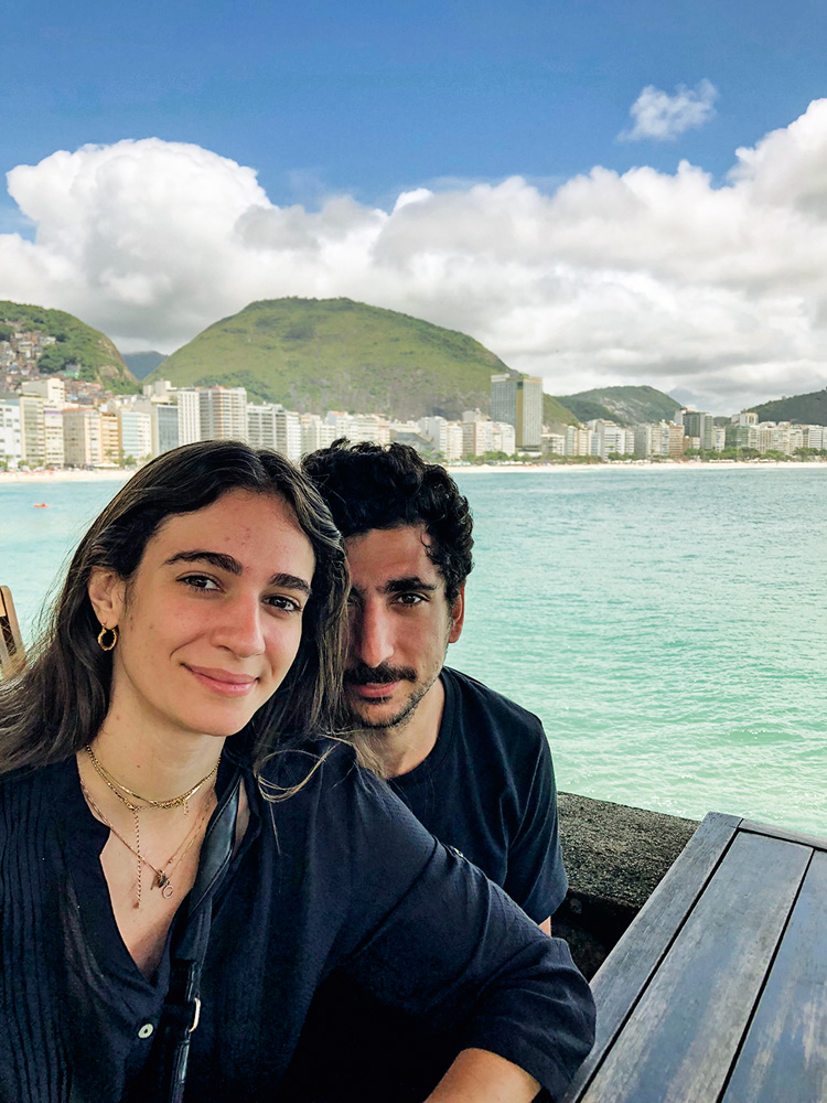 Meu Louco Amor – Camila & Armand (2).JPG Foto de Camila e o noivo. Ambos são brancos, de cabelos e olhos escuros. Ela tem o cabelo liso e comprido e ele o cabelo enrolado e barba. Eles posam para a foto em frente à praia de Copacabana. Ambos usam roupas em tons escuros.