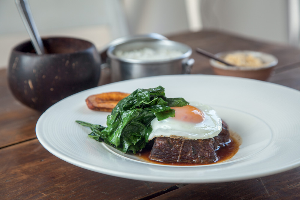 Prato branco com carne bovina, ovo e couve por cima.