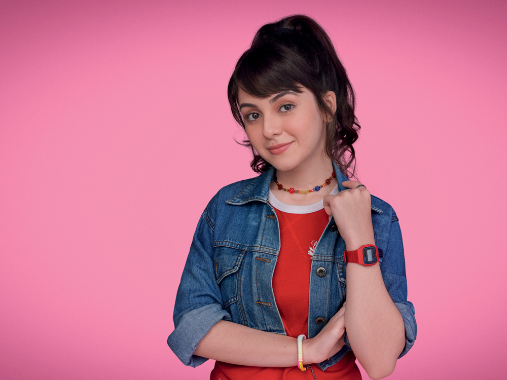 de volta aos 15 – credito Gustavo Zylbersztajn (3).jpg Imagem mostra mulher com jaqueta jeans sobre camiseta vermelha. Ela posa em frente a um fundo rosa.
