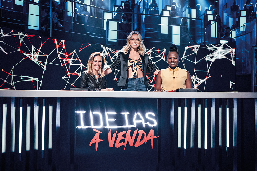 Imagem mostra três mulheres atrás de balcão iluminado com o logo escrito "Ideias à venda"