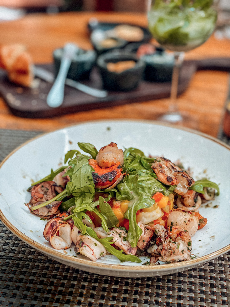 A Figueira Rubaiyat Salada rica em folhas de rúcula e frutos do mar diversos é servida em prato de louça de cor clara