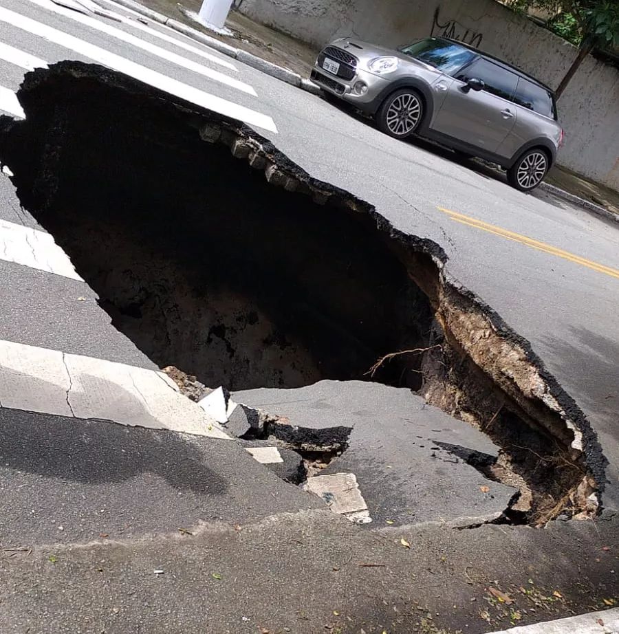 Imagem mostra asfalto com enorme buraco, próximo de faixa de pedestres