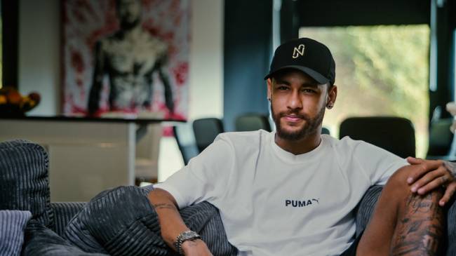 neymar – credito netflix.jpg Imagem mostra homem de camiseta branca e boné preto, sentado em sofá.