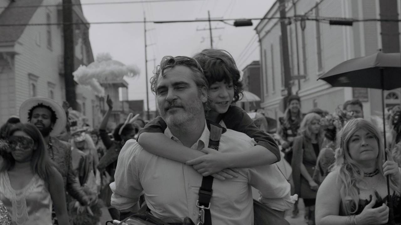Um homem carrega um jovem menino nas costas; felizes, eles estão em uma passeata com uma multidão ao fundo