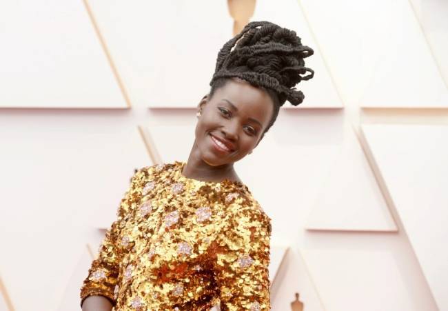 Lupita Nyong'o, de vestido dourado, sorrindo no tapete vermelho