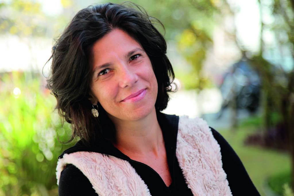 Andrea Barata Ribeiro – crédito para Carlos Vechi.jpg Ana é uma mulher branca, magra de cabelos curtos e escuros e olhos também escuros. Ela posa para a foto com um sorriso e usa uma camisa preta e um colete felpudo bege.