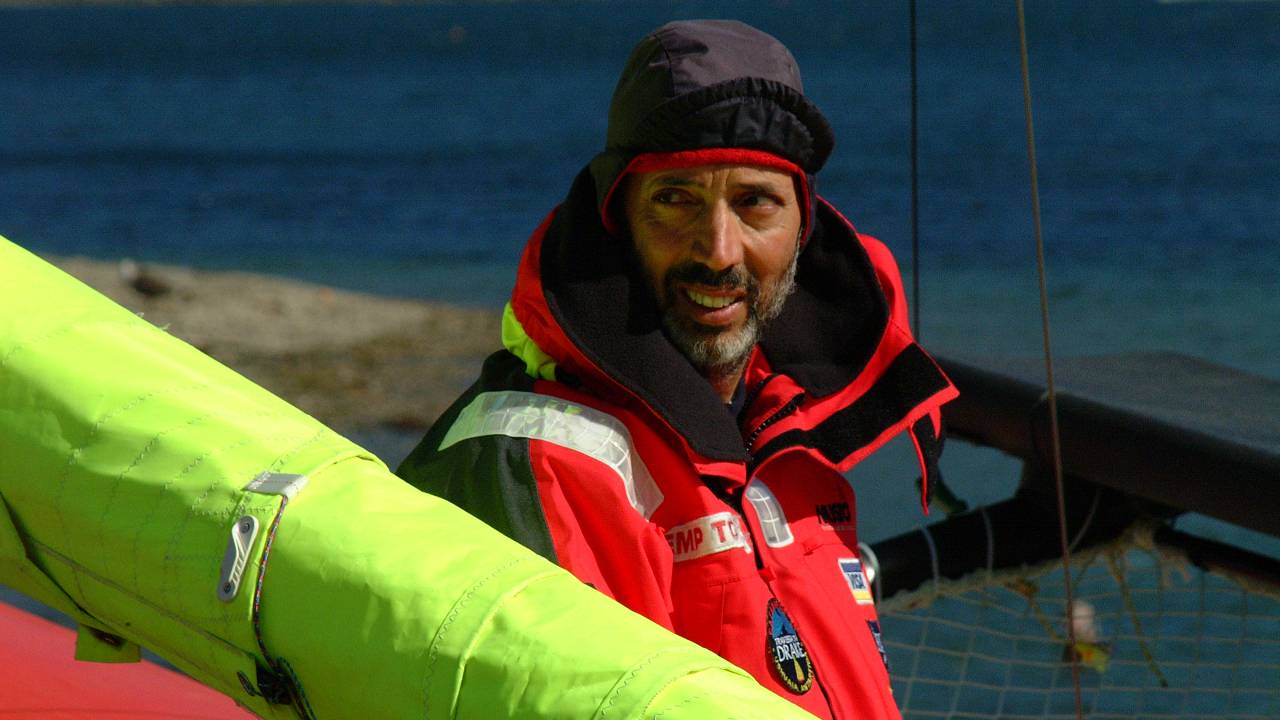 O velejador Beto Pandiani sorri no barco e olha para a esquerda. Ele veste casaco vermelho com capuz.