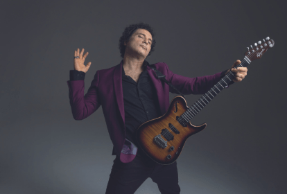 Imagem mostra homem de terno roxo segurando uma guitarra