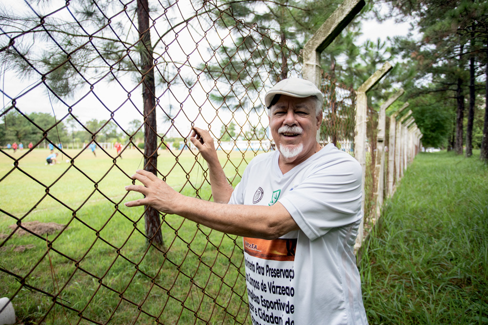 TERRENOCAMPODEMARTE19.jpg Senhor negro sorri ao lado da grade de um campo de futebol gramado