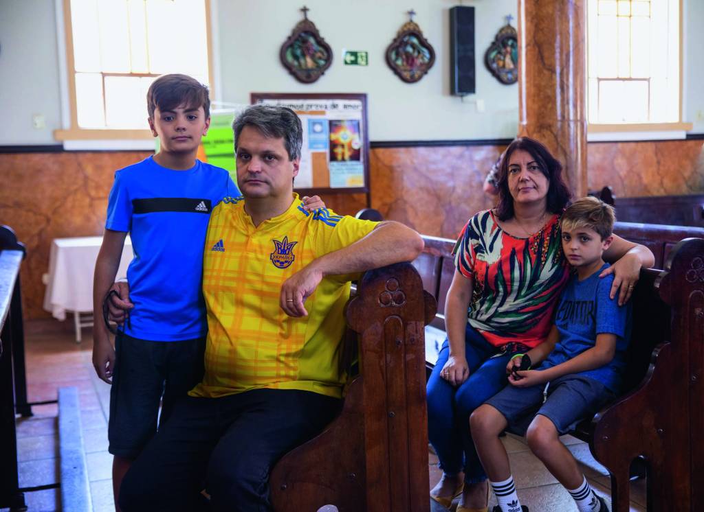 Vila Zelina – Alexandre Captia Imagem mostra família - um casal e dois filhos - sentados em bancos de igreja.