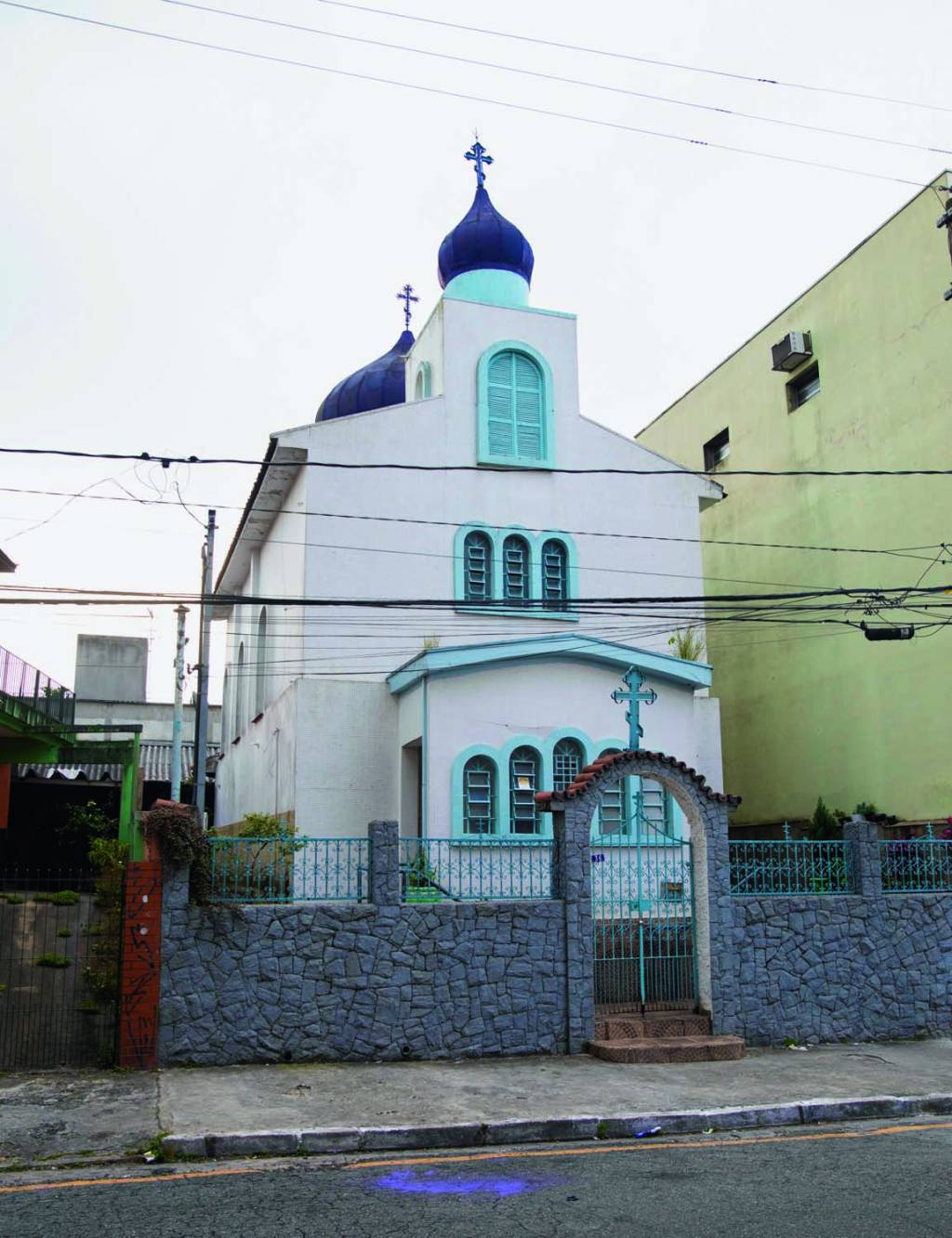 Vila Zelina – templo russo Imagem mostra templo com paredes brancas e detalhes em azul. No terraço, cruzes sobre formas cônicas.