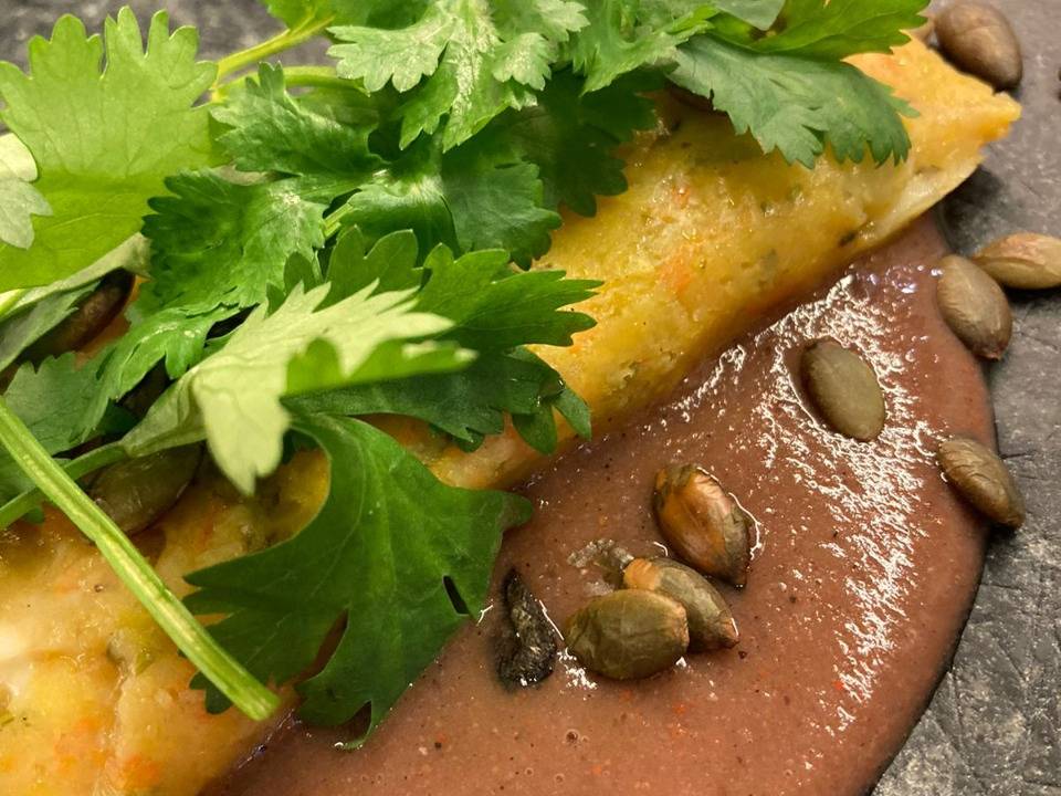 Cuscuz paulista servido em prato de cor escura junto de caldo de feijão e salsa