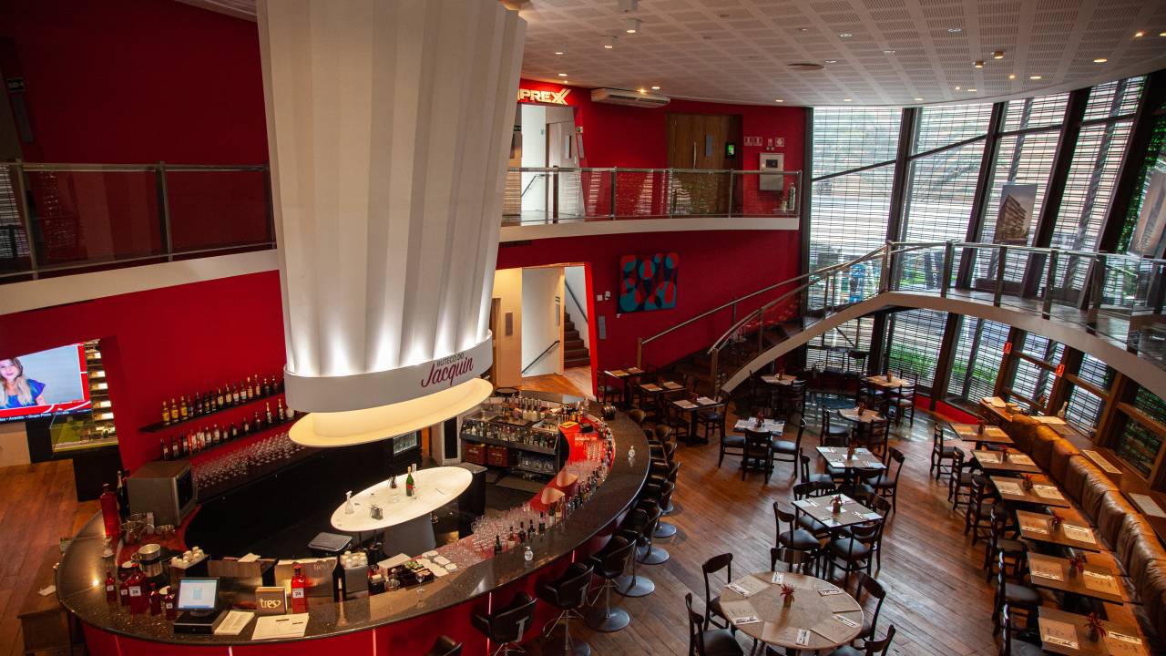 Ambiente de bar decorado em cores vermelhas, com um extenso balcão e uma grande réplica de um chapéu de chef no centro